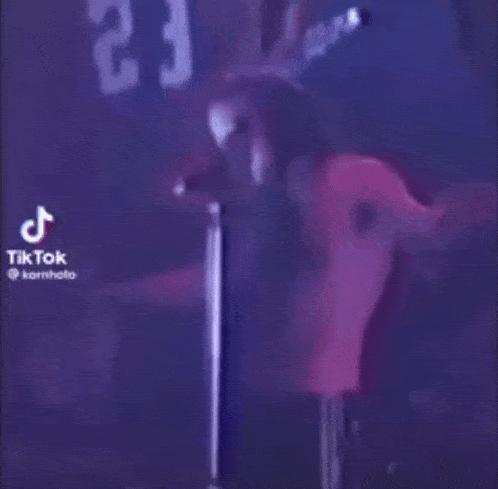 a man is singing into a microphone while standing on a stage in a dark room .