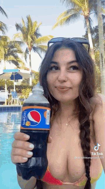 a woman in a bikini is holding a bottle of pepsi next to a pool .