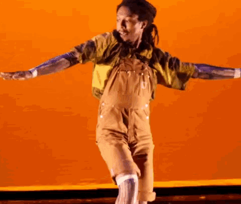 a man wearing overalls and a yellow shirt is dancing on a stage