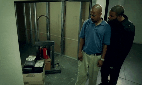two men are standing in a room with boxes of money and a fire extinguisher on the floor