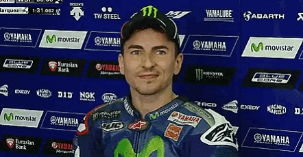 a man wearing a yamaha jacket stands in front of a wall of ads
