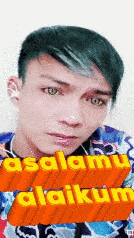 a man with green hair and ear buds says " asalamu alaikum " on an orange background
