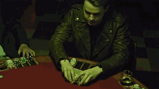 a man in a leather jacket sits at a poker table