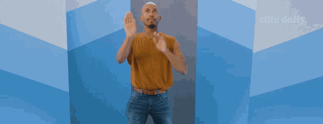 a man in a yellow shirt is standing in front of a blue wall with the elite daily logo on it