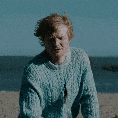 a man wearing a blue sweater stands on a beach
