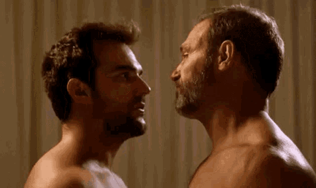 two shirtless men are kissing each other on the forehead in a room .