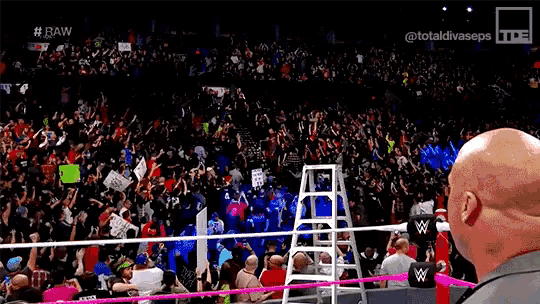 a bald man is standing in front of a crowd of people in a stadium .