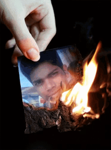 a person is holding a picture of a young boy in front of a fire