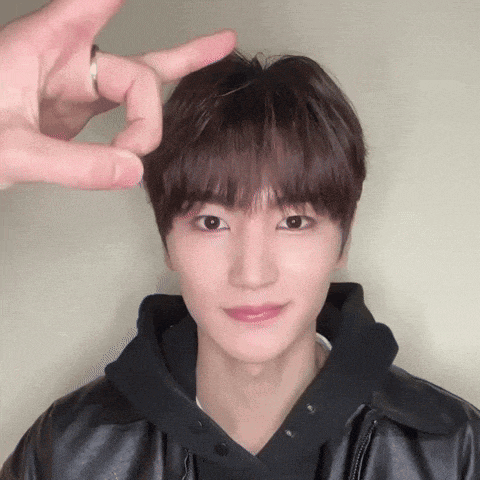 a young man wearing a black jacket and a black hoodie is making a peace sign with his hands