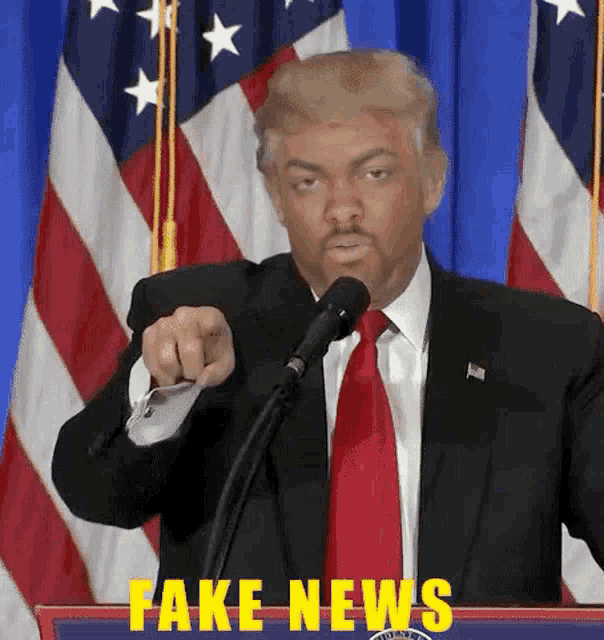 a man in a suit and tie is pointing at a microphone with fake news written on the podium behind him