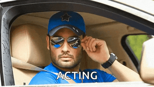 a man wearing sunglasses and a blue hat is sitting in a car and the word acting is on the window