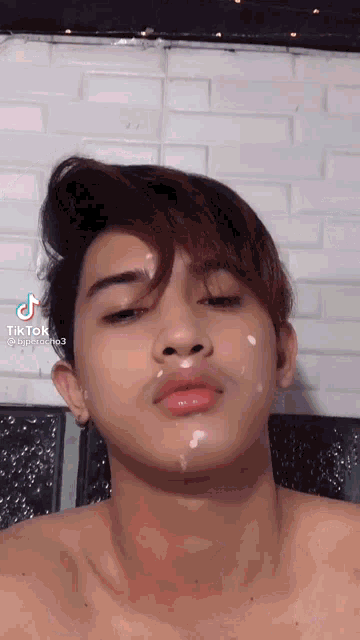a young man without a shirt is making a funny face with a brick wall behind him