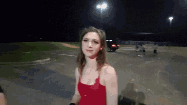 a woman in a red tank top is standing in a parking lot at night