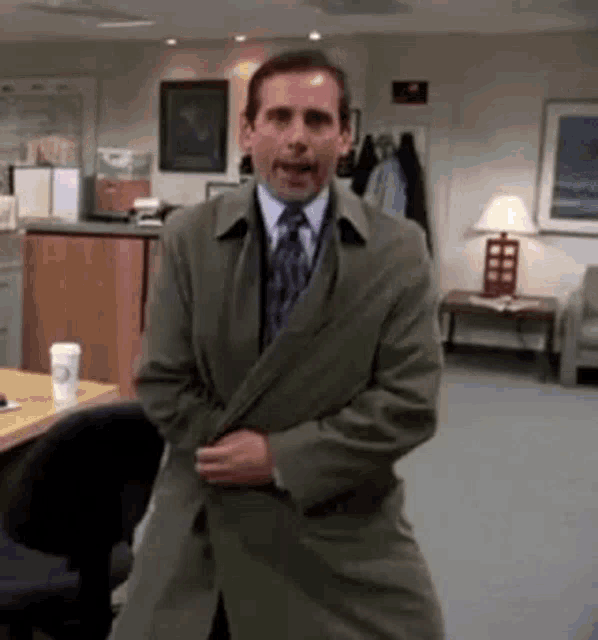 a man in a trench coat and tie is standing in a room in an office .