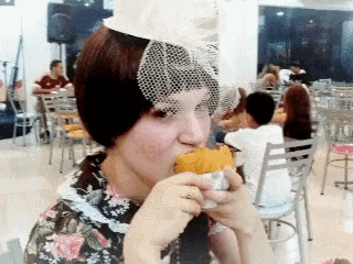 a woman with a veil on her head is eating a hamburger