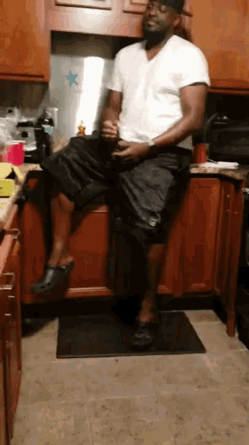 a man sits on a cabinet in a kitchen with a star on the refrigerator