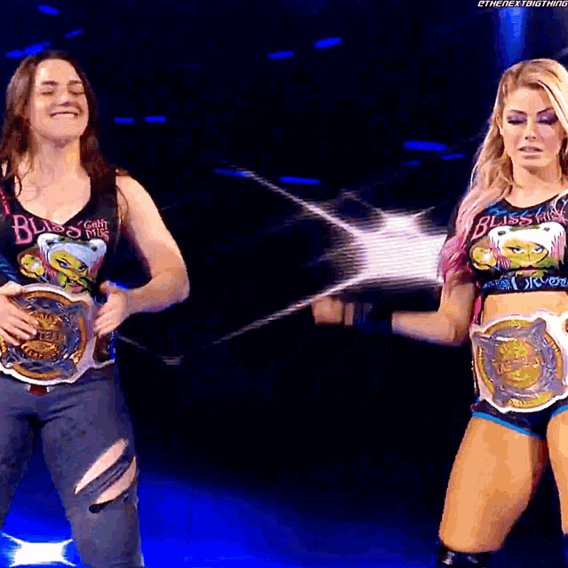 two female wrestlers with bliss on their shirts are standing on a stage