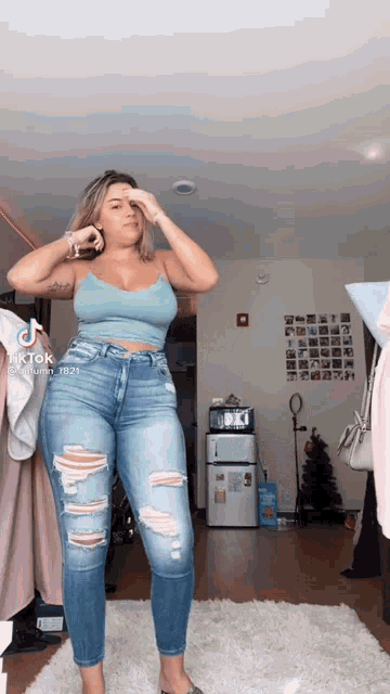 a woman wearing ripped jeans and a blue tank top is standing in a room .