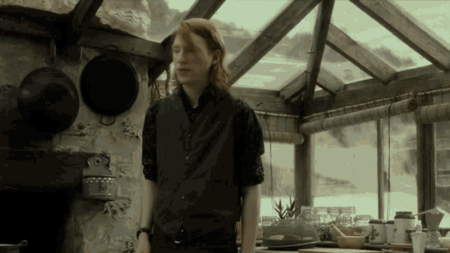 a man in a black vest is standing in a kitchen with pots and pans hanging from the ceiling