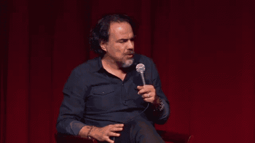 a man is sitting in front of a red curtain holding a microphone .