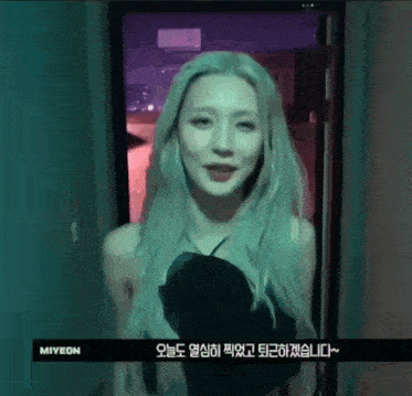 a woman with long blonde hair is standing in front of a door with foreign writing on it .