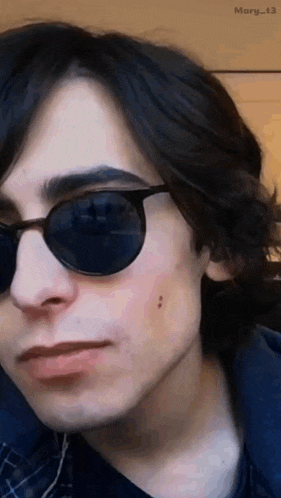 a close up of a young man wearing sunglasses and a plaid shirt .