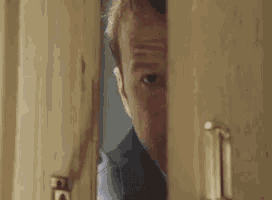 a man is smiling while peeking through a door .