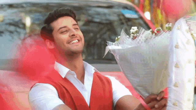 a man is holding a bouquet of flowers in front of a red car