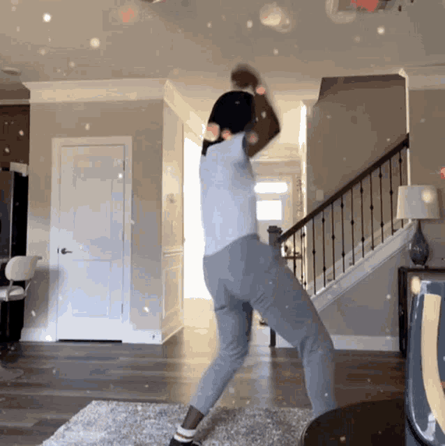 a person is dancing in a living room with a staircase in the background