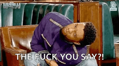 a man is sitting on a couch holding his stomach and says `` the fuck you say '' .