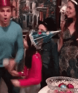 a group of people are standing around a table with a woman wearing a party hat on her head .