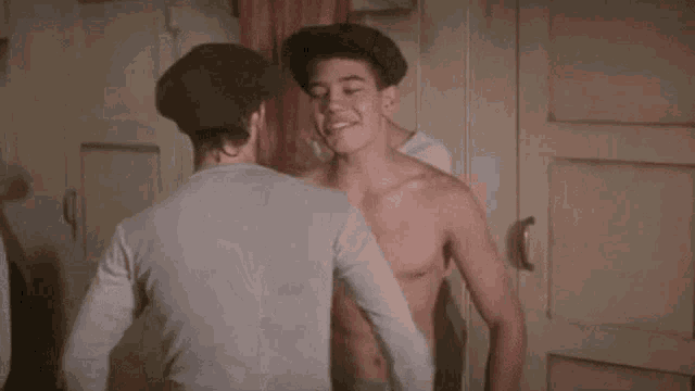 a shirtless man is standing next to another shirtless man in a locker room .