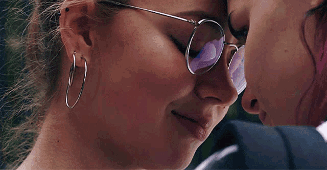 a woman wearing glasses and hoop earrings looks down at another woman 's face