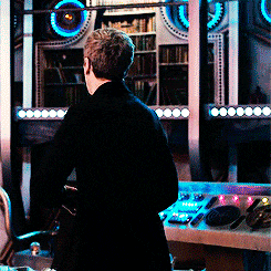 a man in a black coat is standing in front of a control panel in a dark room