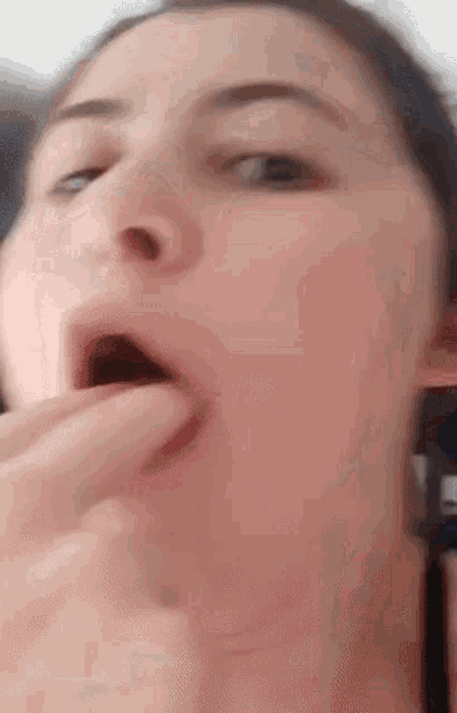 a close up of a woman 's face with her mouth open and her fingers in her mouth .