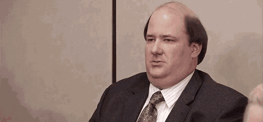 a bald man in a suit and tie is sitting at a table in an office with his eyes closed .