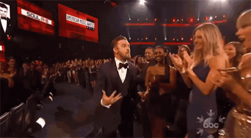 a man in a tuxedo is dancing on a stage in front of a crowd of people applauding .