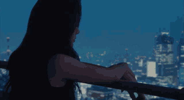a woman leans on a railing looking out over a city at night