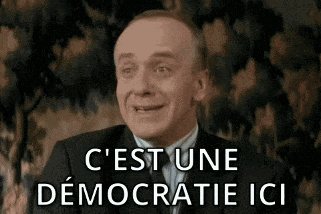 a man in a suit and tie is smiling with the words c ' est une democratie ici below him