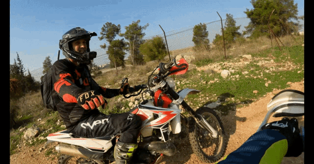 a man riding a dirt bike wearing a helmet and fox gloves