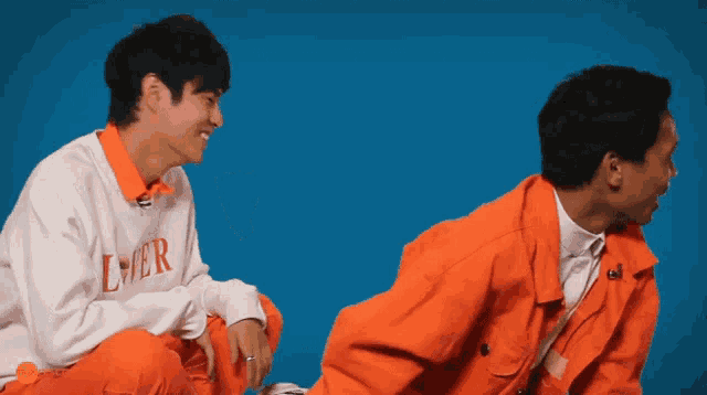 a man wearing an ever sweatshirt sits next to another man in orange