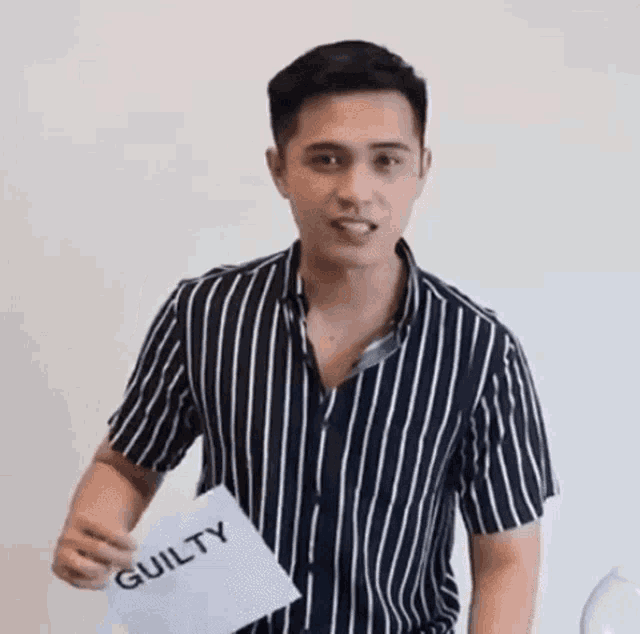 a young man in a striped shirt is holding a piece of paper that says guilty .