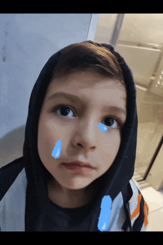 a young boy wearing a hooded jacket has a blue tear on his face