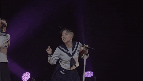 a girl in a sailor uniform sings into a microphone with a red band around her arm