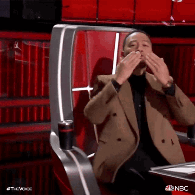 a man in a brown jacket is sitting in a chair with his hands on his face .