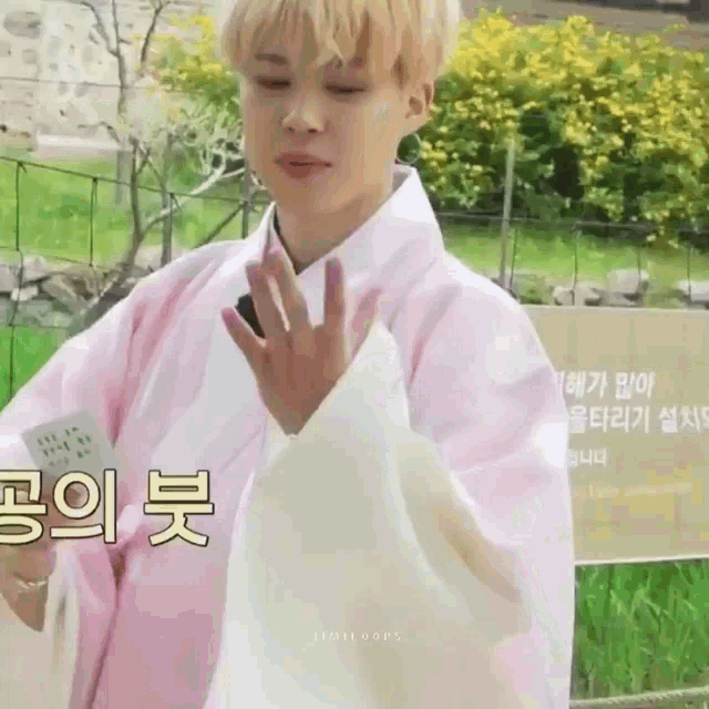 a young man wearing a pink and white kimono is waving his hand in front of a sign in korean .
