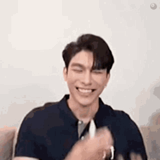 a man in a blue shirt is smiling while sitting on a couch with his eyes closed and his hands in his pockets .