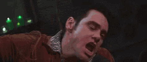 a man is yawning while sitting in a chair in a dark room with his mouth open .