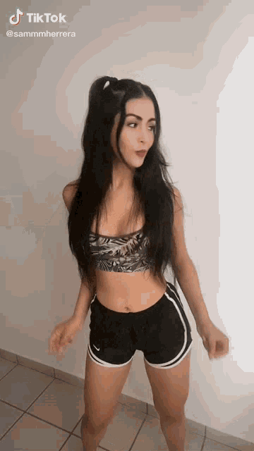 a woman in a sports bra and shorts is dancing on a tiled floor .