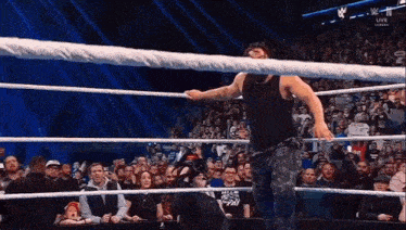 a man in a black tank top is standing in a wrestling ring with a crowd watching .